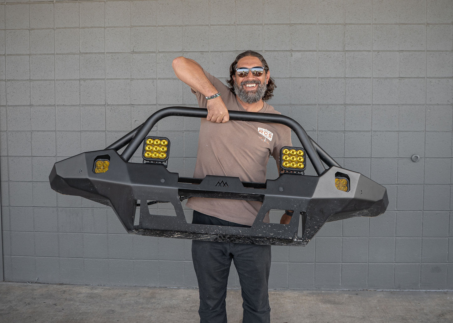 Man lifting the 2024 4th Gen Toyota Tacoma Backwoods Adventure Mods Hi-Lite Overland hybrid aluminum high clearance Front Bumper with Prerunner Bull Bar with one hand